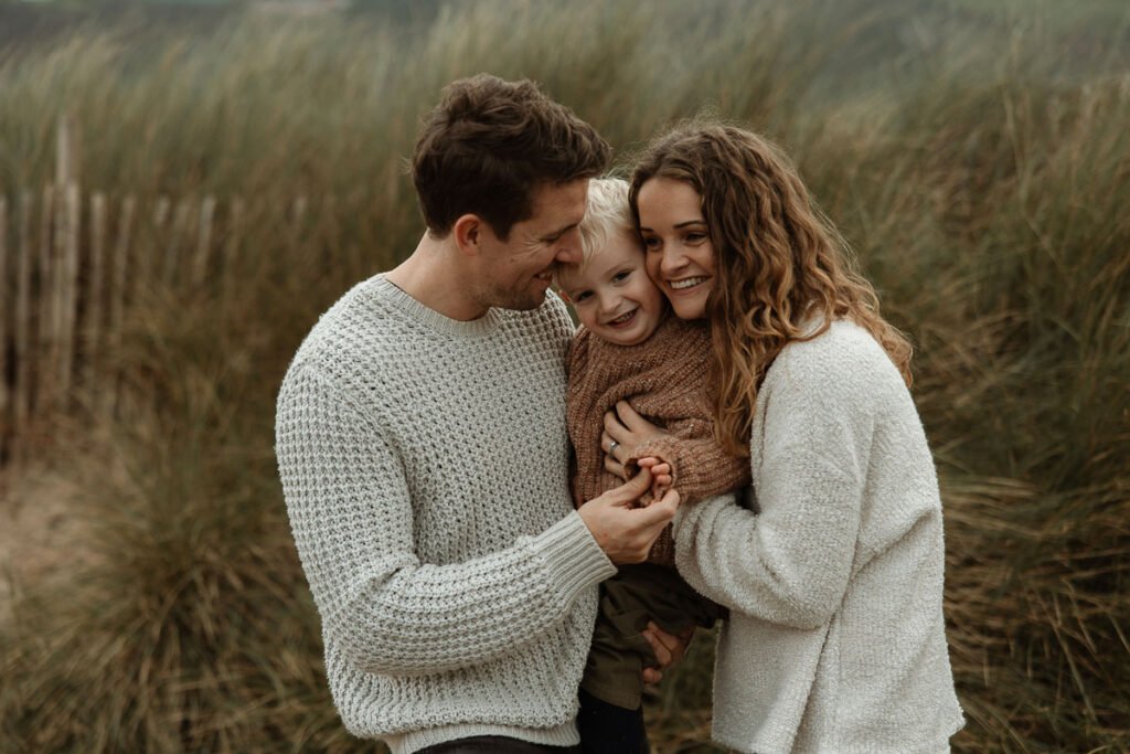 parents tickling their young son in the sand dunes on Bantam Beach, Devon