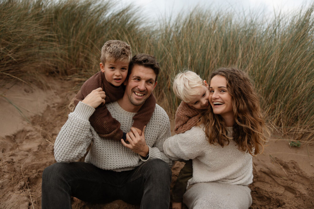 Portrait of a family of four hugging in the sand dunes on Bantham Beach, Devon