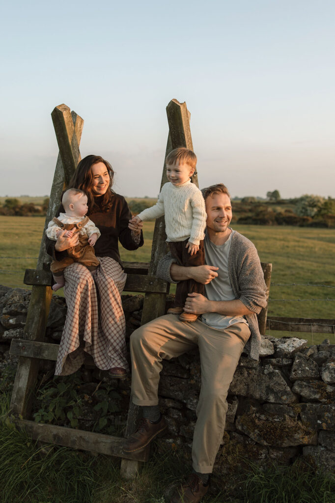 portrait of a family with parents and two children sitting on a wall, smiling at sunset